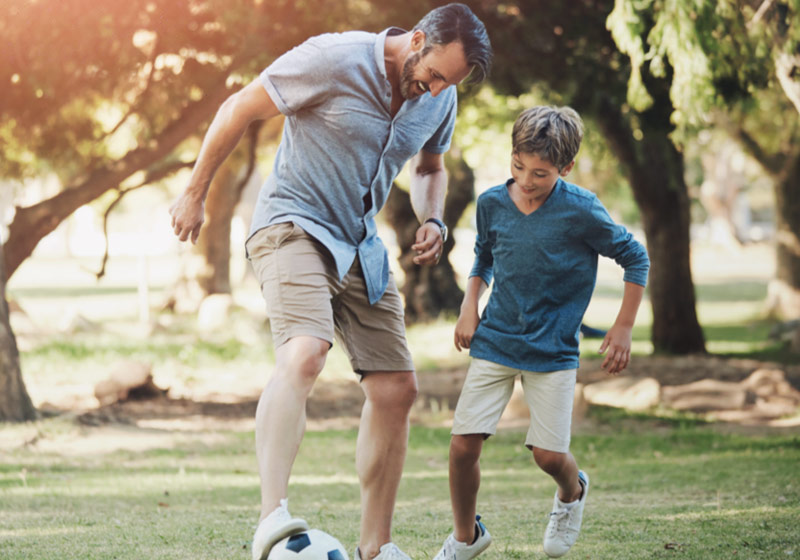 Padre e hijo jugando con una pelota de fútbol.