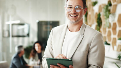 Hombre sonriendo hacia la cámara con una tablet en la mano.