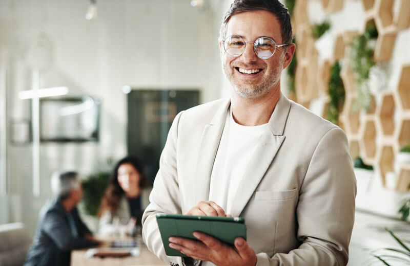 Hombre sonriendo hacia la cámara con una tablet en la mano.