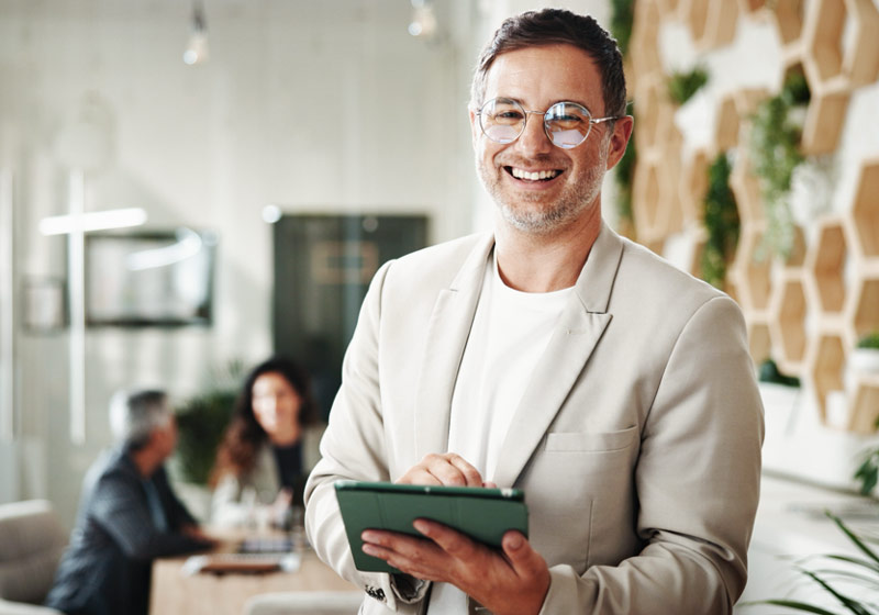 Hombre sonriendo hacia la cámara con una tablet en la mano.