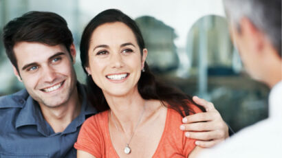 Pareja sonriendo y abrazada frente a un asesor financiero.