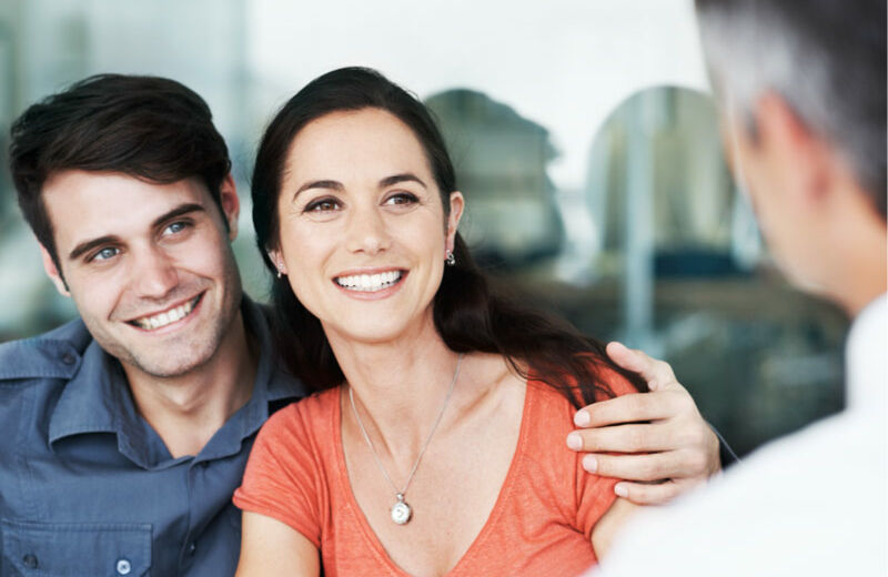 Pareja sonriendo y abrazada frente a un asesor financiero.
