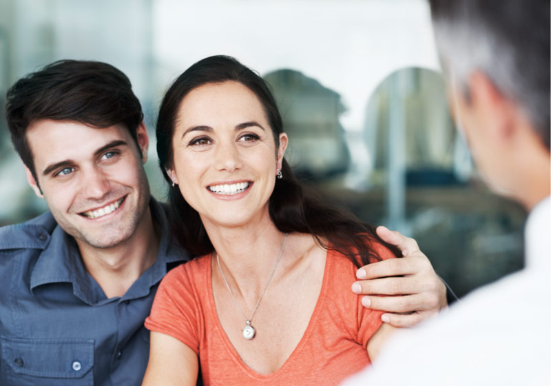 Pareja sonriendo y abrazada frente a un asesor financiero.