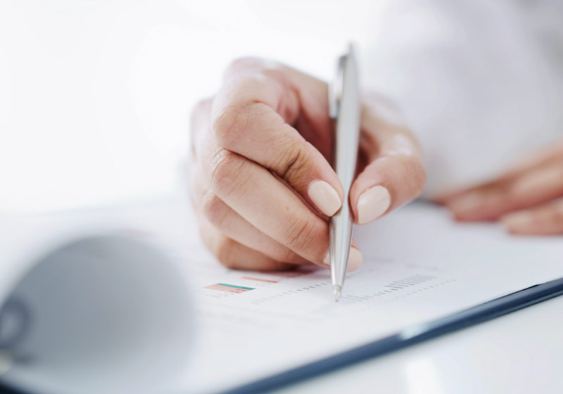 Primer plano de la mano de una mujer firmando un documento.