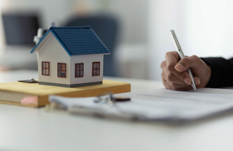 Maqueta de una casa y una persona firmando unos documentos.