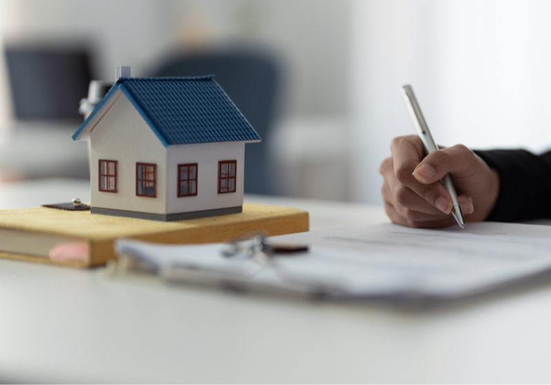 Maqueta de una casa y una persona firmando unos documentos.